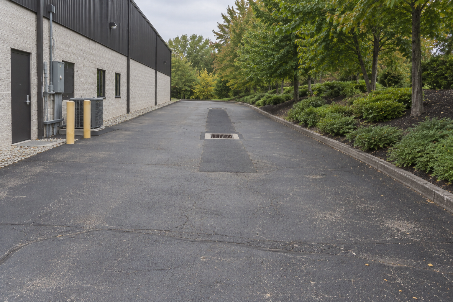 Two catch basins and an asphalt reinstatement strip beside a white block commercial building